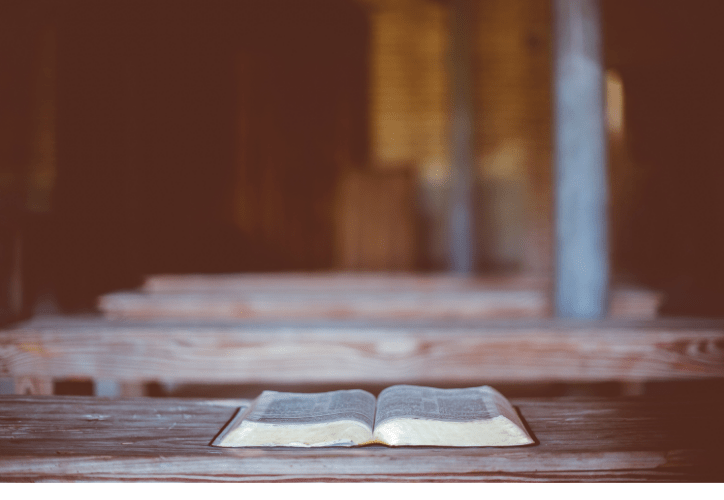 Image of an open Bible on a wooden table with a blurred background.