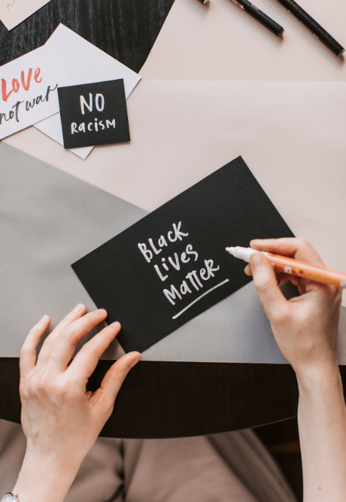 Image of white hands writing Black Lives Matter on a black piece of paper